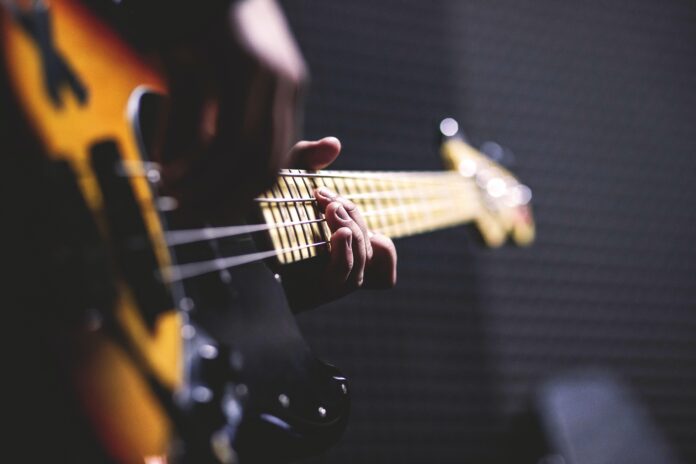 person playing sun burst electric bass guitar in bokeh 96380 scaled